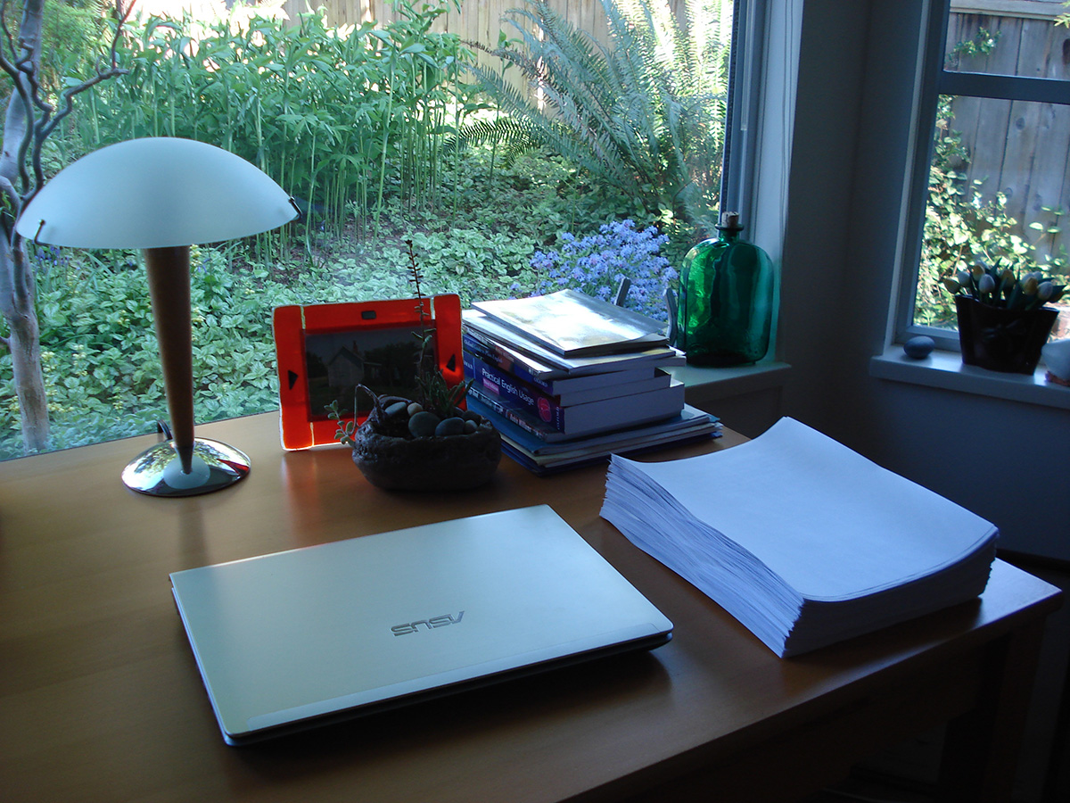 The first draft of The Broken Places sitting on a desk, with a lamp and a large window behind