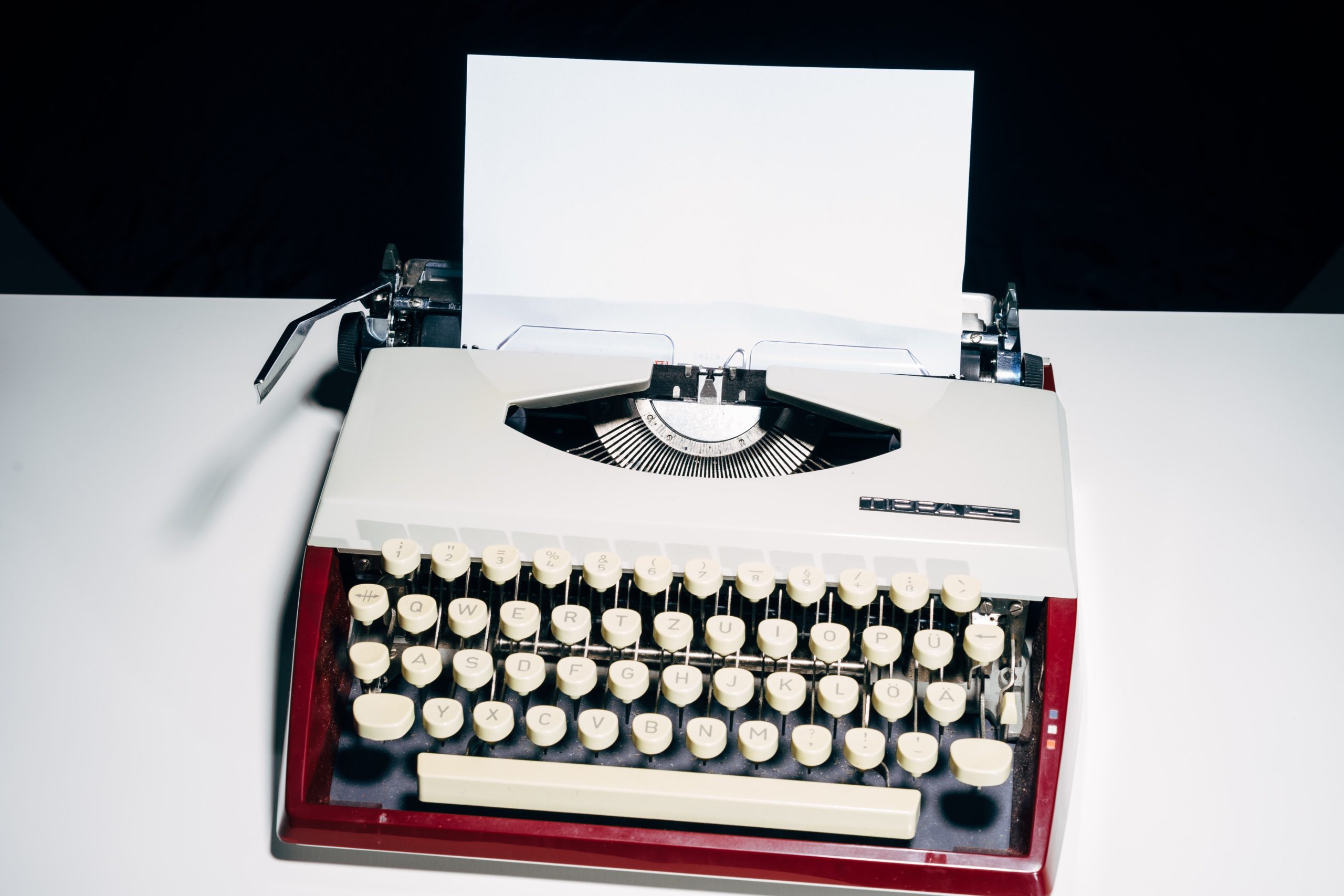 A red and white typewriter with a piece of paper coming out of the top