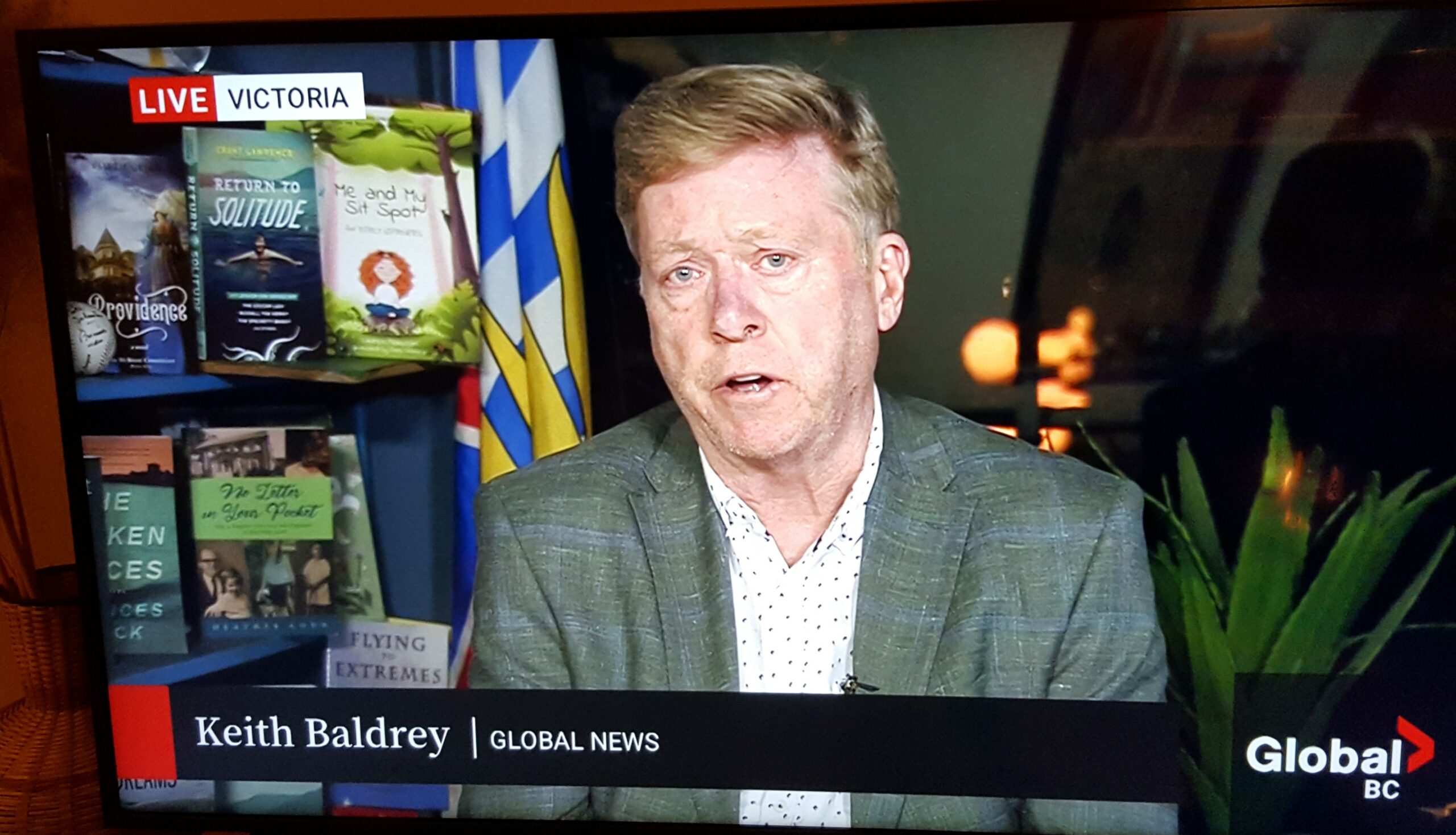 Global TV's Victoria correspondent Keith Baldrey, reporting live from Victoria, with bookshelves behind him that feature BC books, one of which is The Broken Places