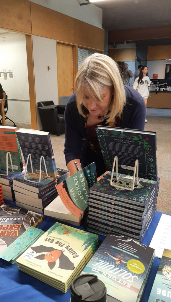 Frances signing a copy of The Broken Places at the festival's book table, in between the displays of books for sale.