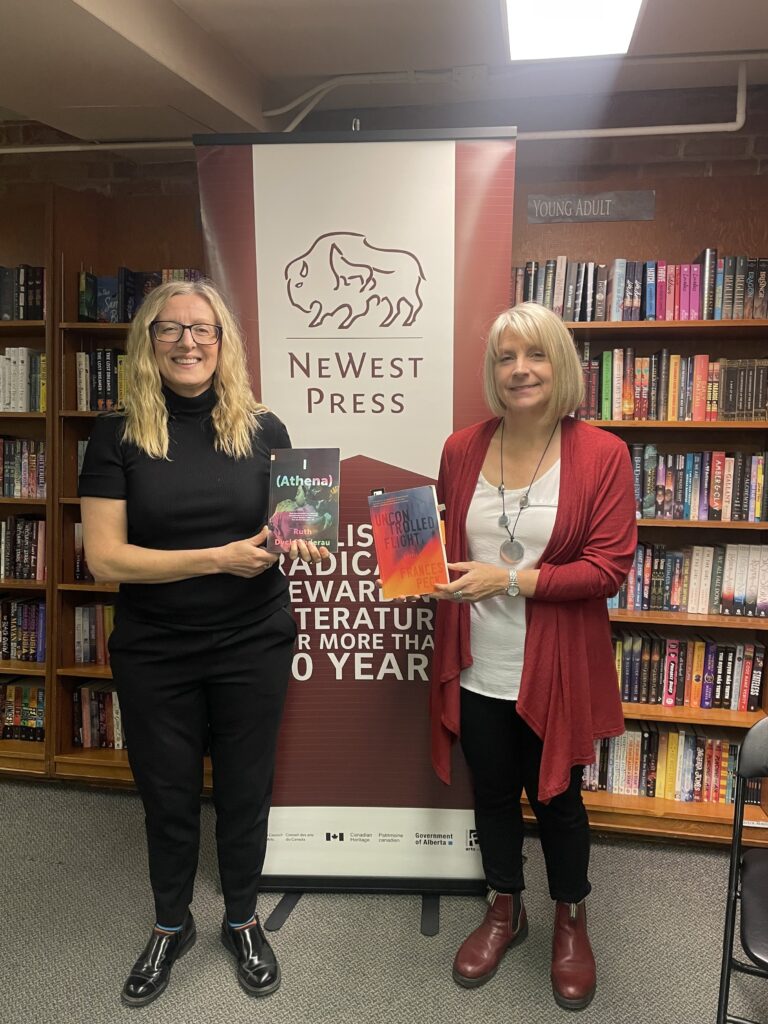A background of bookshelves at Audreys Books. Standing in front of them are (left) Ruth DyckFehderau and (right) Frances Peck, holding their novels. Between them is a stand-up banner for NeWest Press.